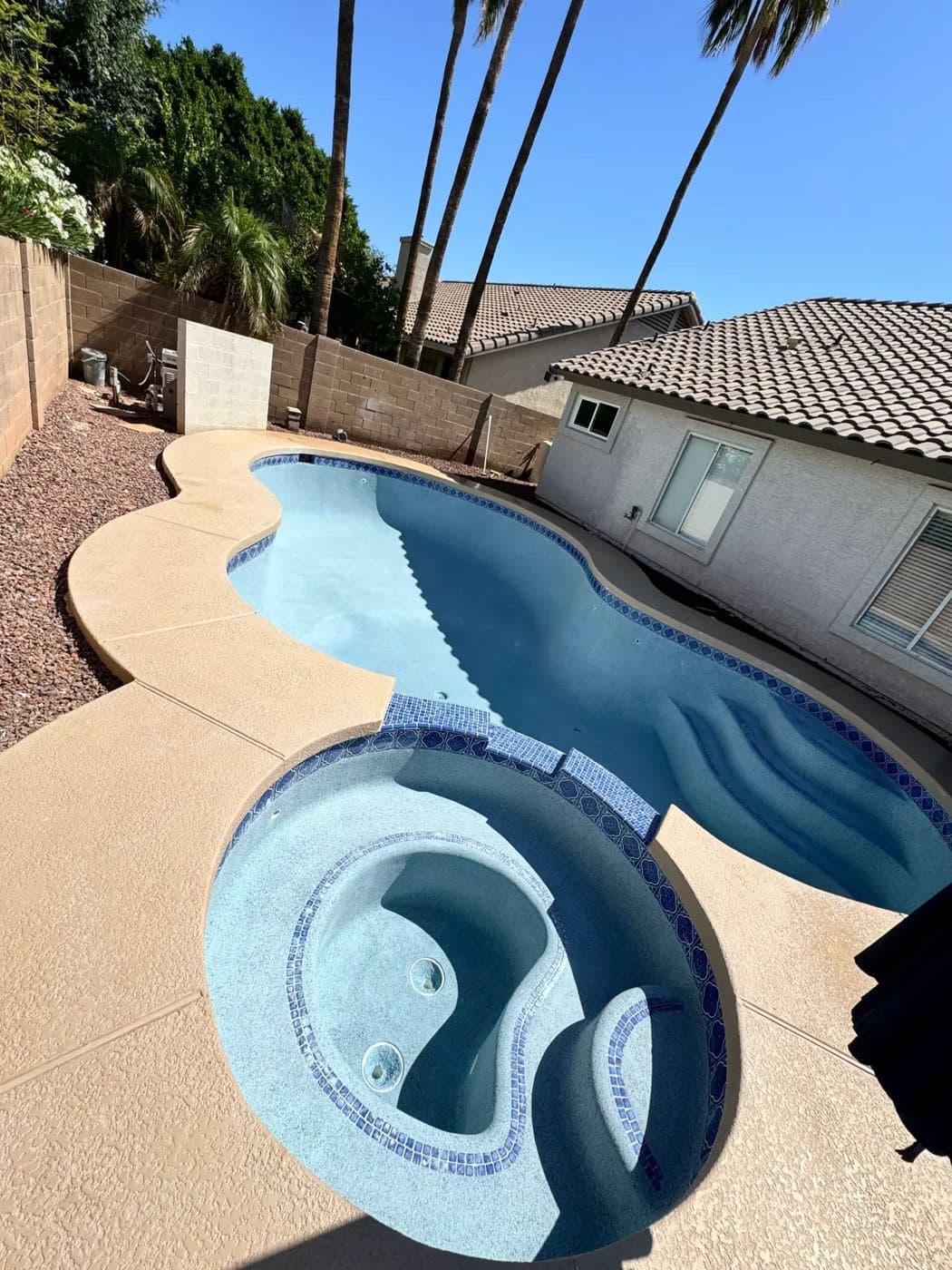 Curved pool with an attached round spa, blue tile trim and a tan deck