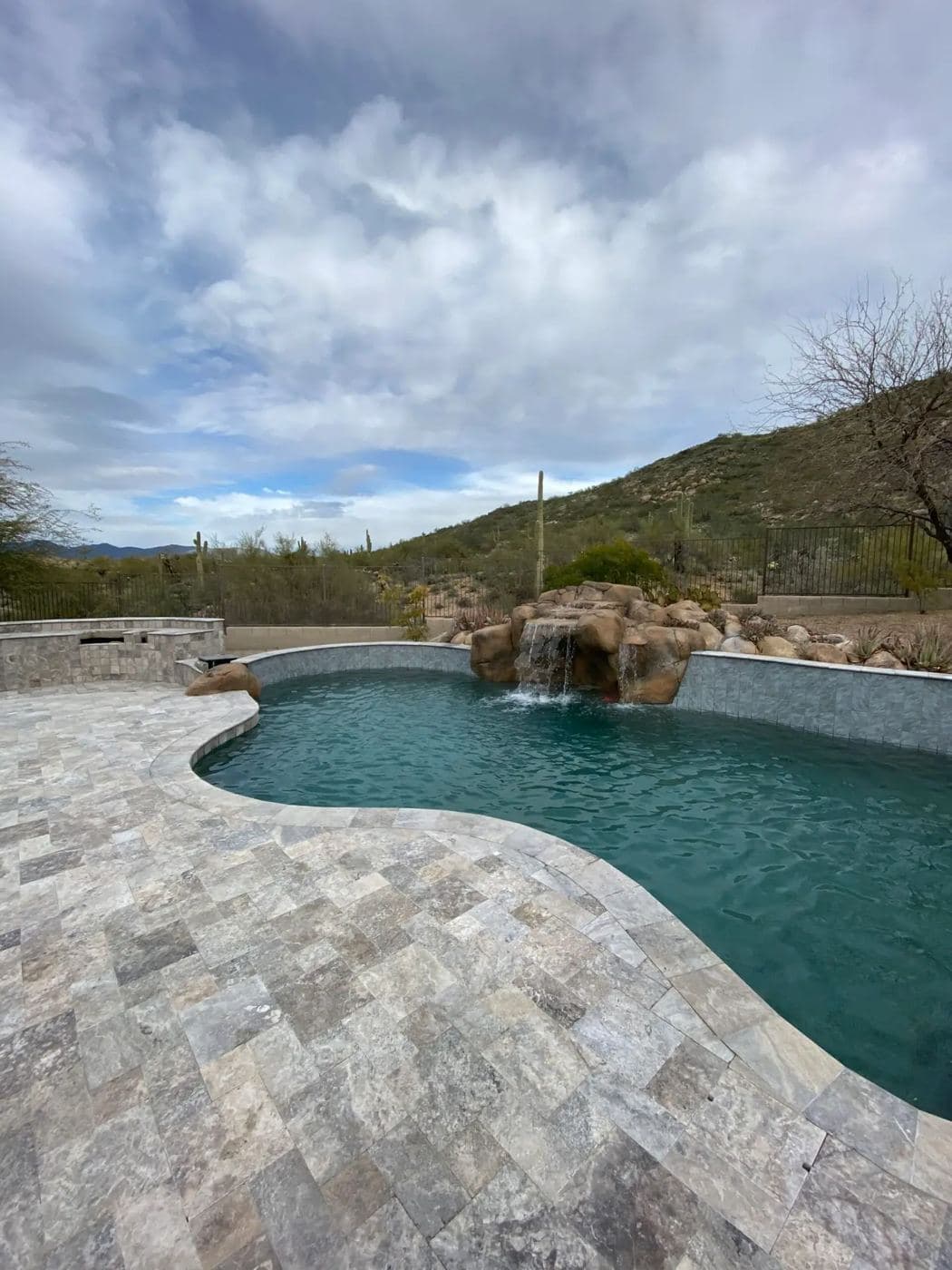 A finished curved pool with a stone waterfall against Arizona hills