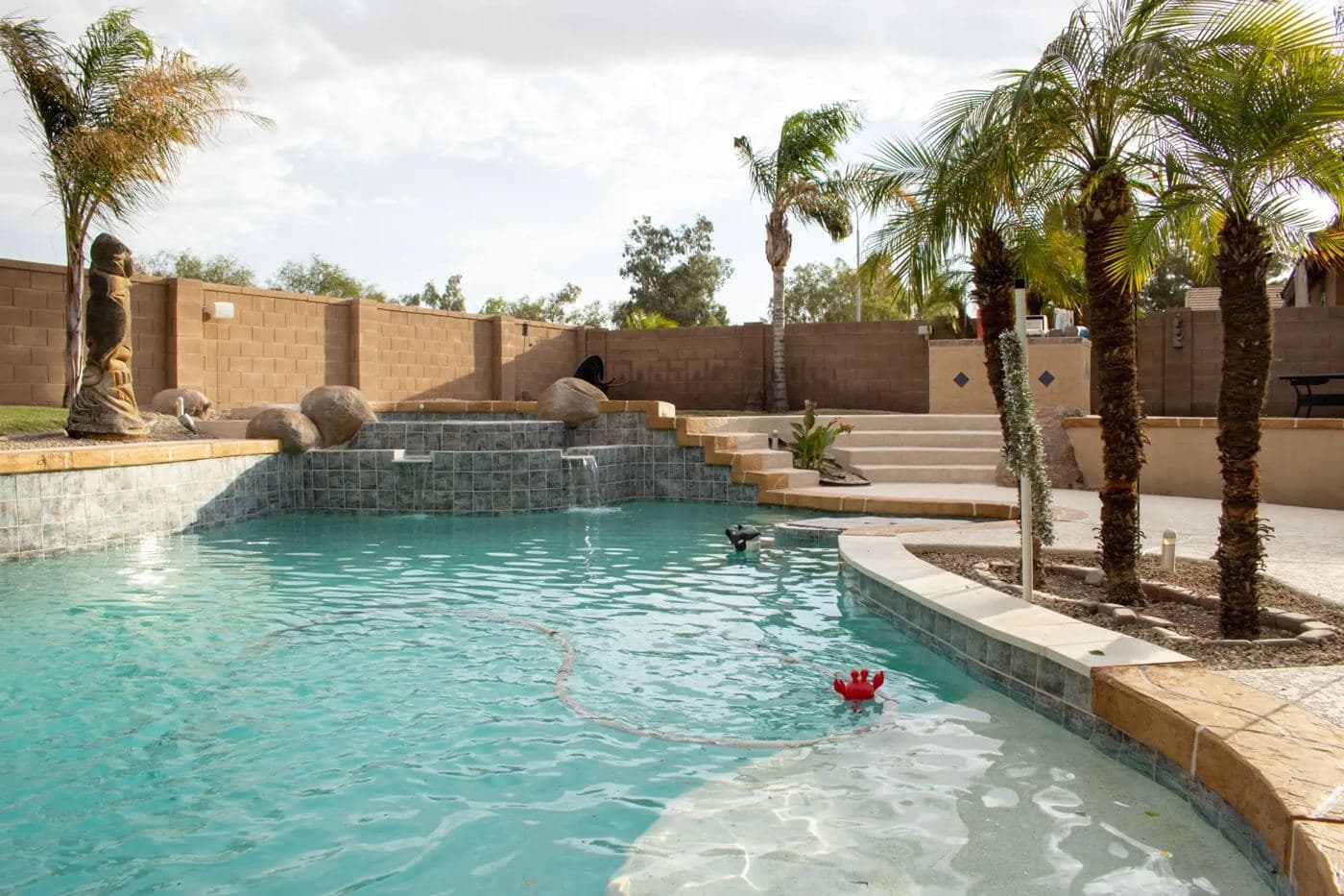 Curved pool with a rock waterfall, a shallow beach entry and palm trees
