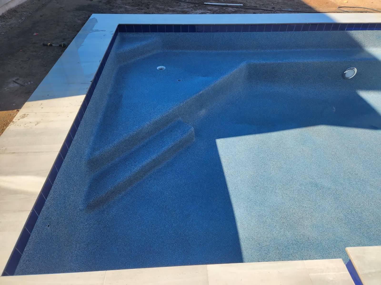 Empty pool with a fresh blue finish, steps, a bench and dark blue tile